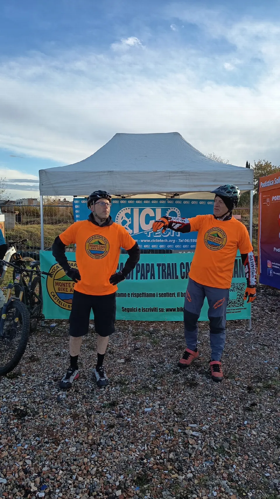 Due soci in maglia arancione davanti al gazebo dello stand Ciclo