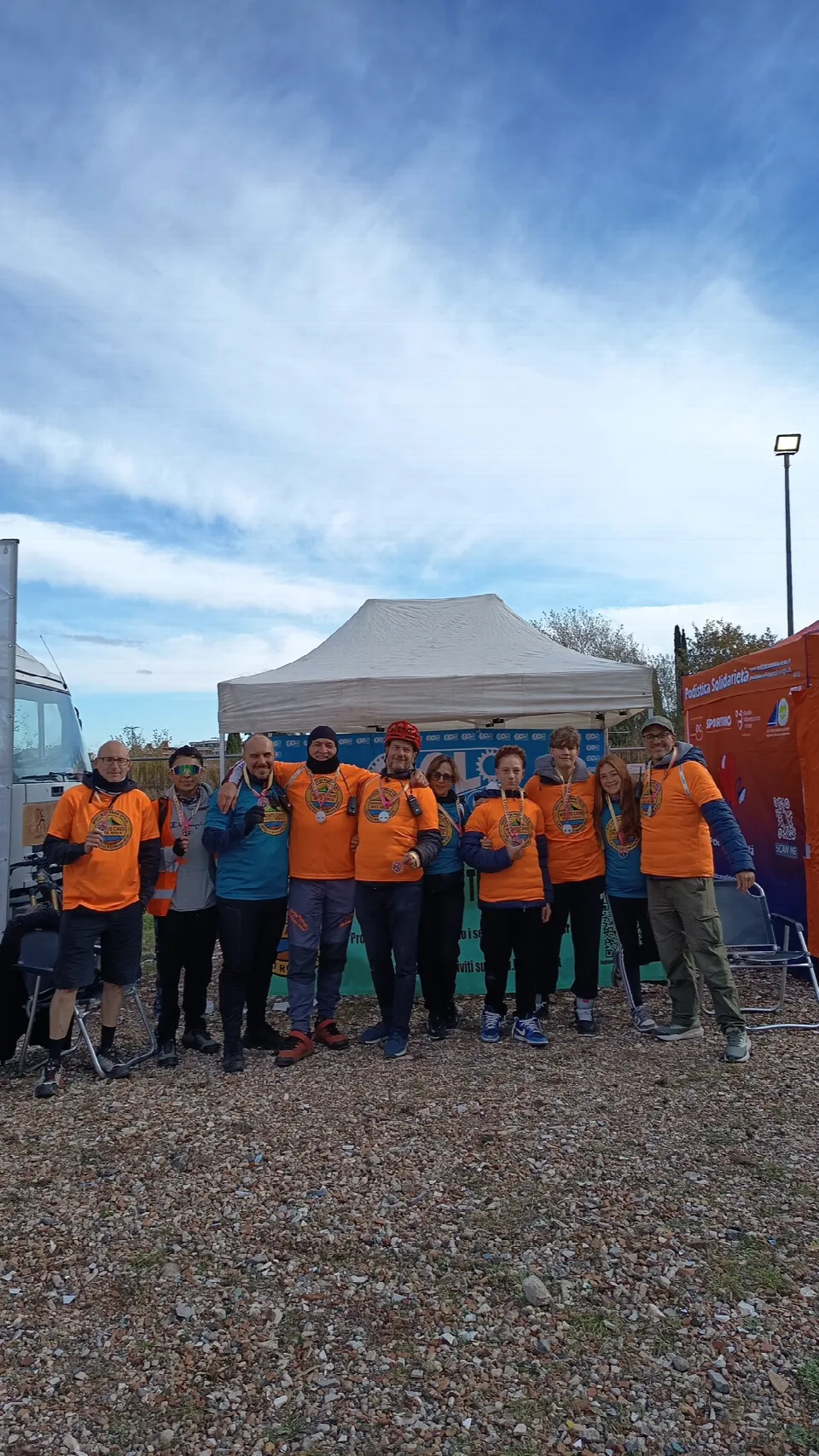 Foto di gruppo dei soci in maglia arancione davanti al gazebo