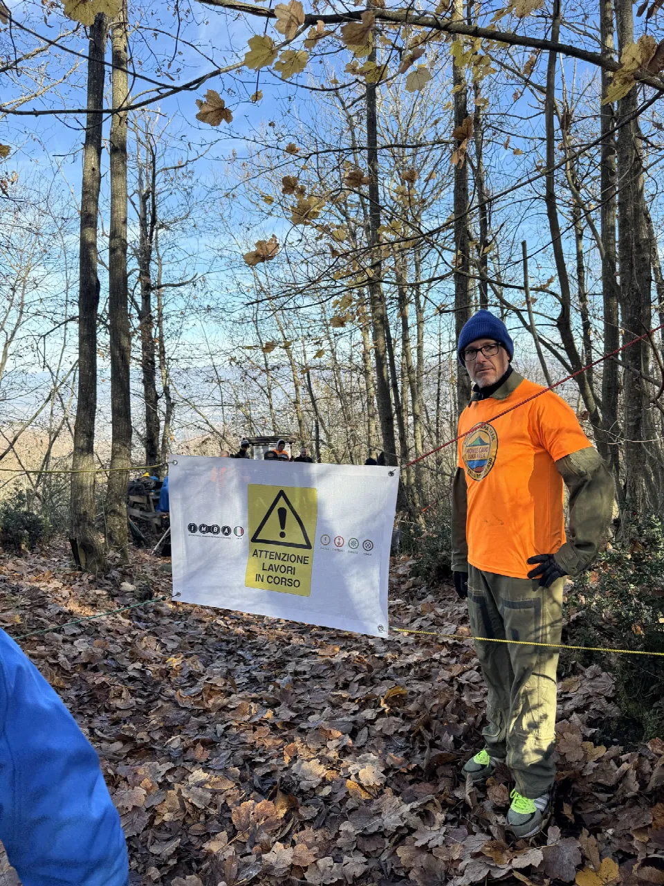 Volontario in arancione accanto al cartello «Attenzione lavori in corso» su un sentiero